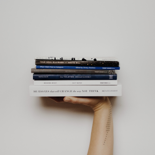 A hand of a person holding 7 different books