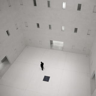 A man standing inside a very big gray room with many windows