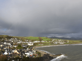 A picture of the countryside with many small houses, the sea, the mountains, and the cloudy sky