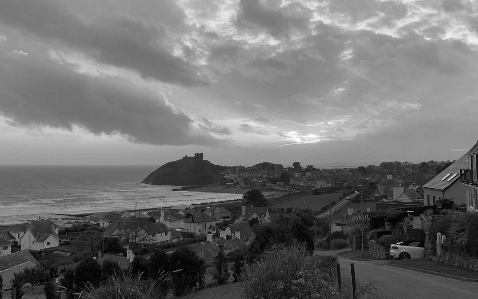 A picture of the countryside with many small houses, roads, bushes, the sea, and the big sky.